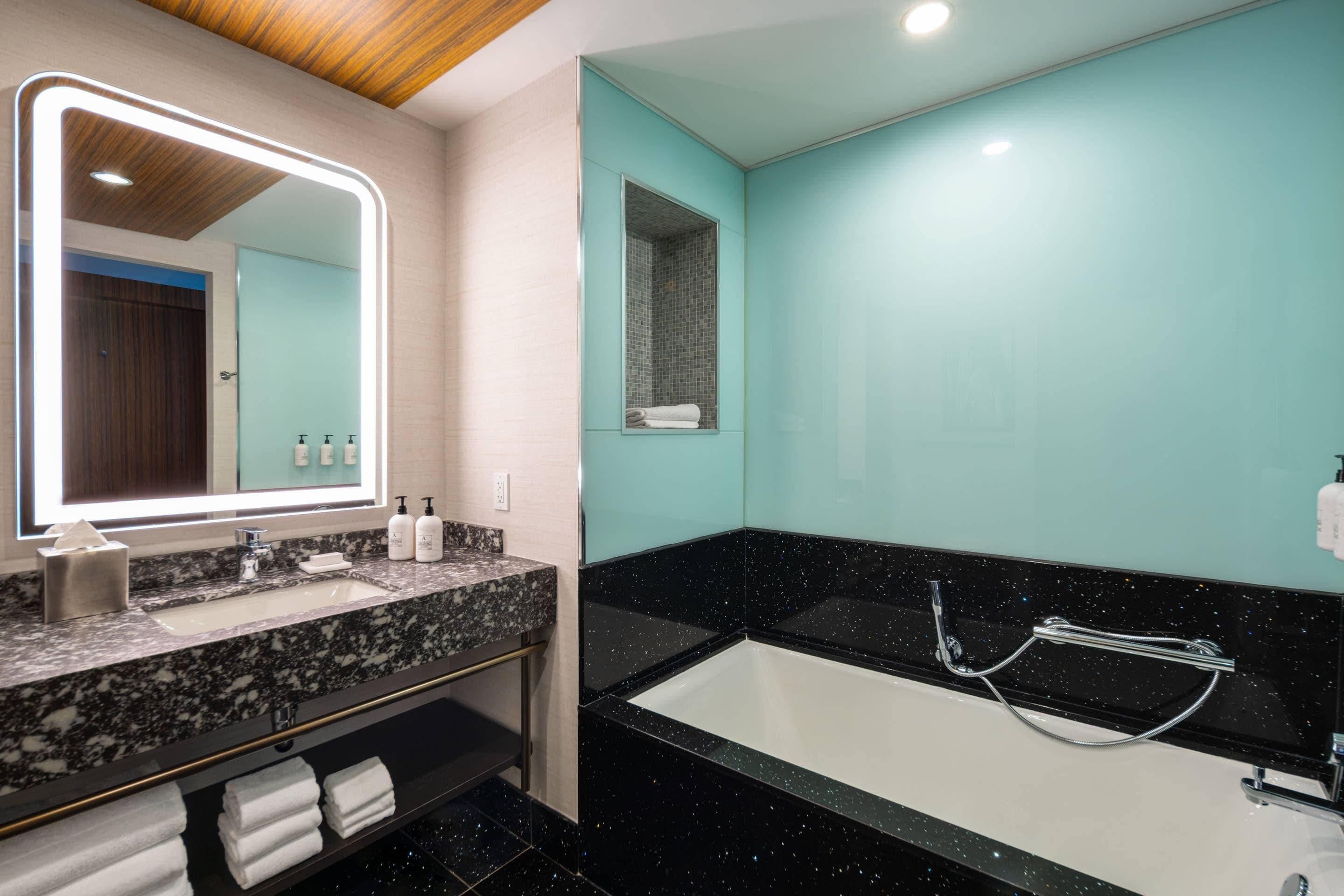 A modern bathroom with a large mirror, a sink, and a bathtub.