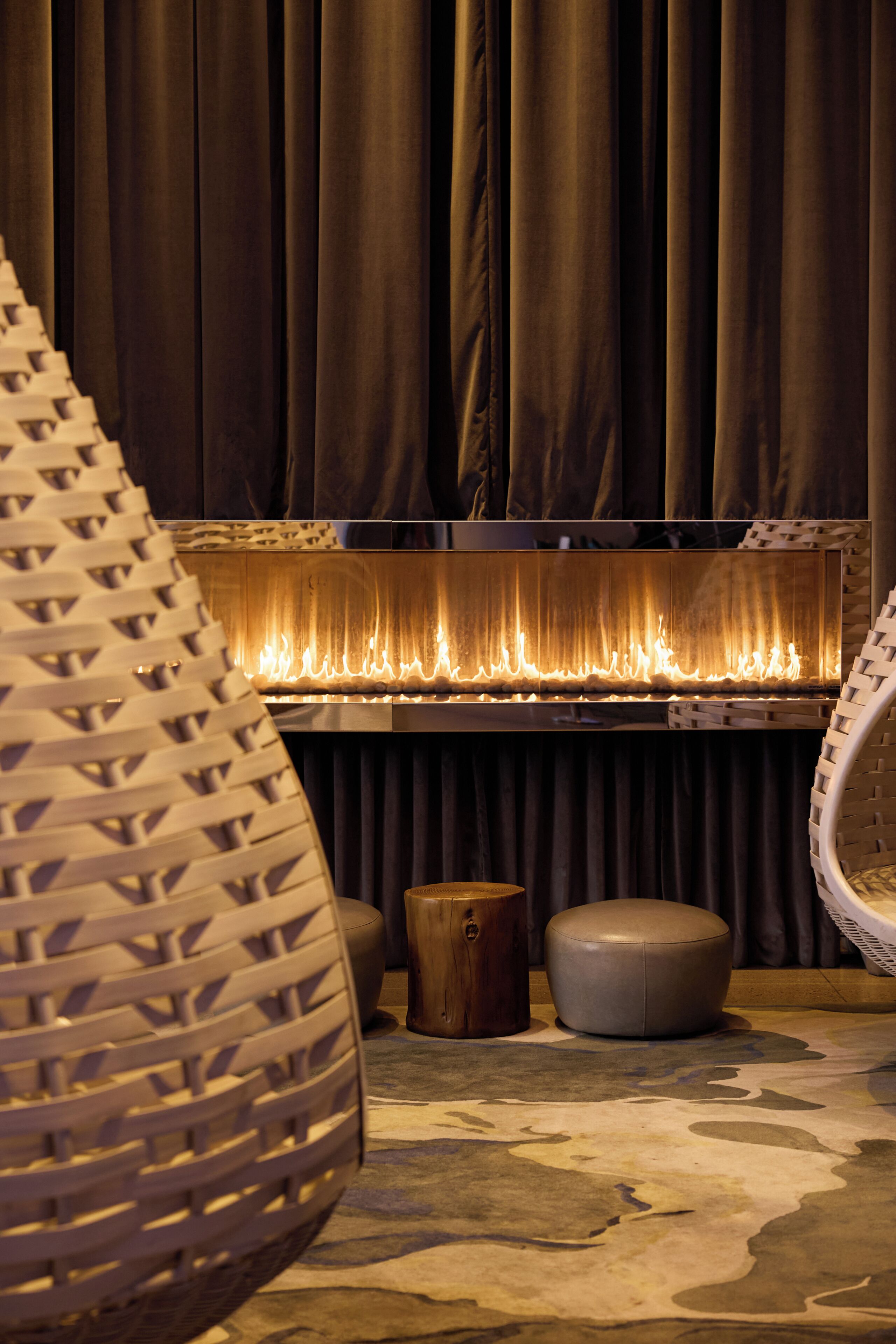 A room with a fireplace, dark curtains, and a patterned rug.
