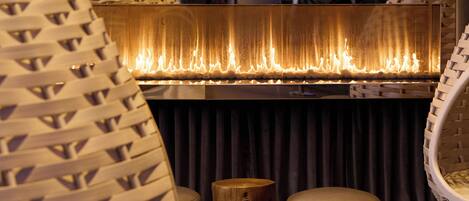 Una habitación con chimenea, cortinas oscuras y una alfombra estampada.