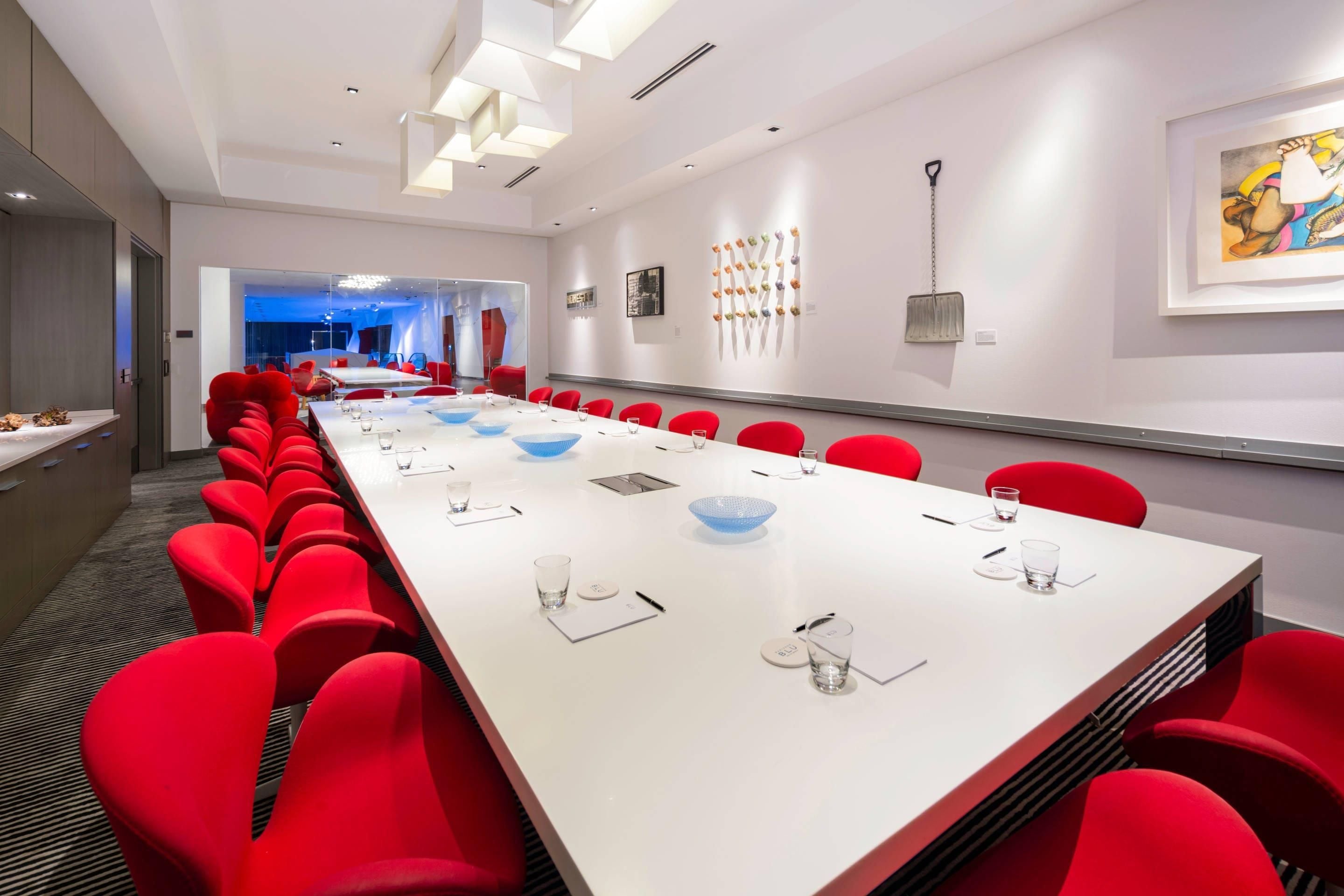 Une salle de conférence dotée d’une longue table, de chaises rouges et d’un plafond au design moderne.