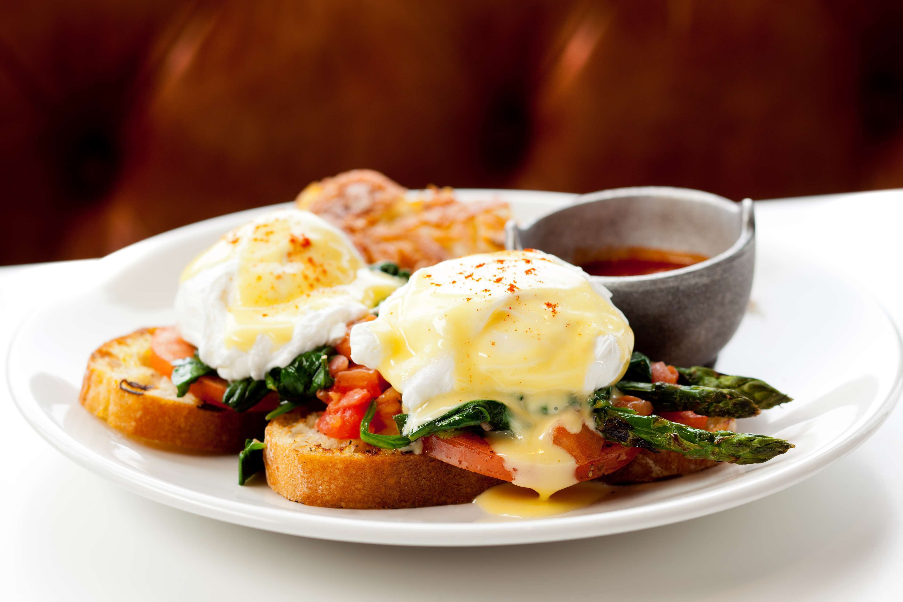 A plate of eggs benedict with hollandaise sauce, asparagus, and tomatoes on toast.
