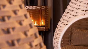 Una silla de mimbre con asiento y respaldo circulares, ubicada frente a una chimenea con llamas visibles.