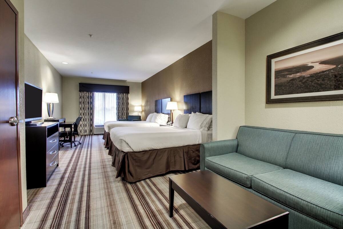 A hotel room with a large bed, a sofa, a desk with a lamp, and a framed picture on the wall.