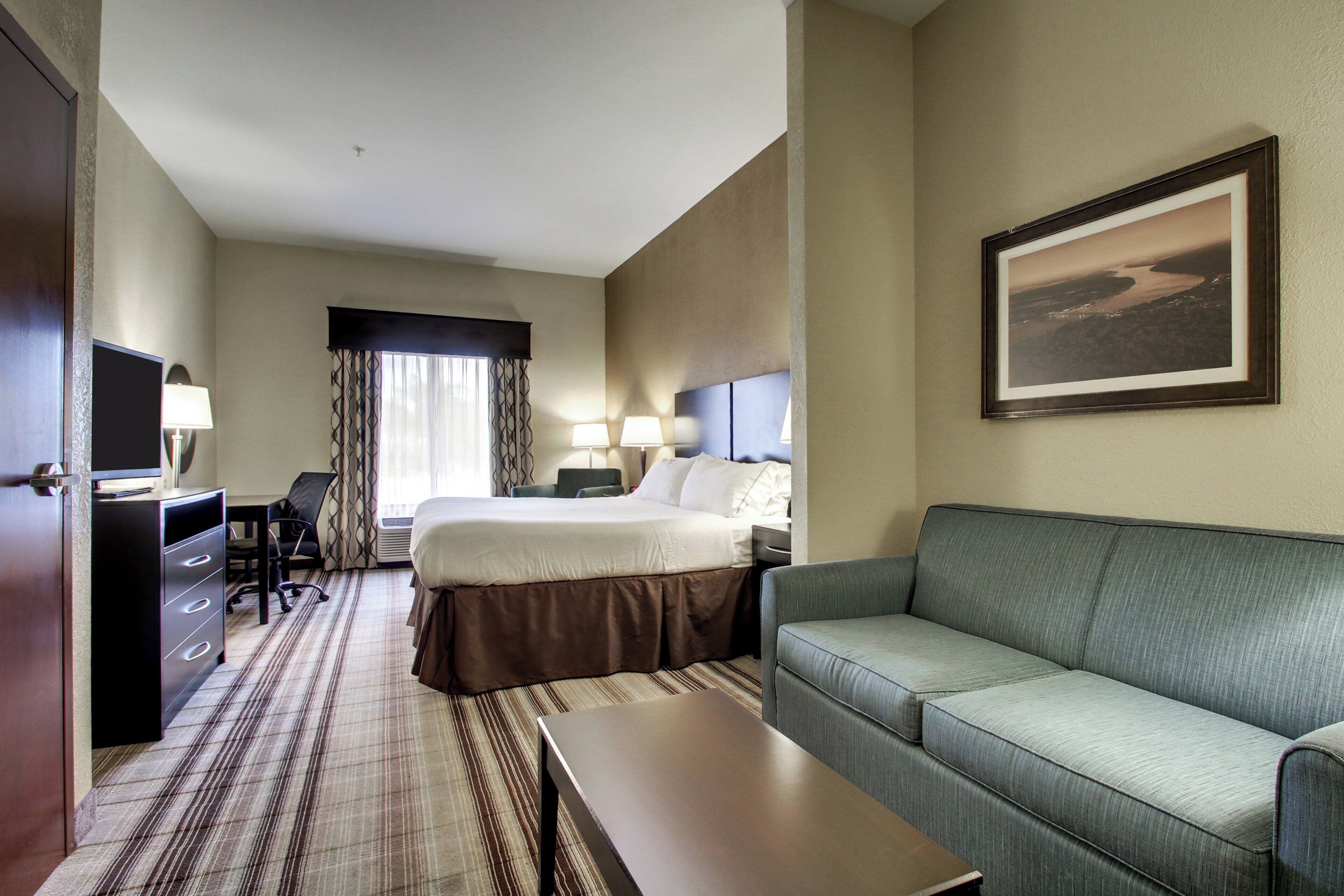A hotel room with a bed, a desk, a chair, a sofa, and a television.
