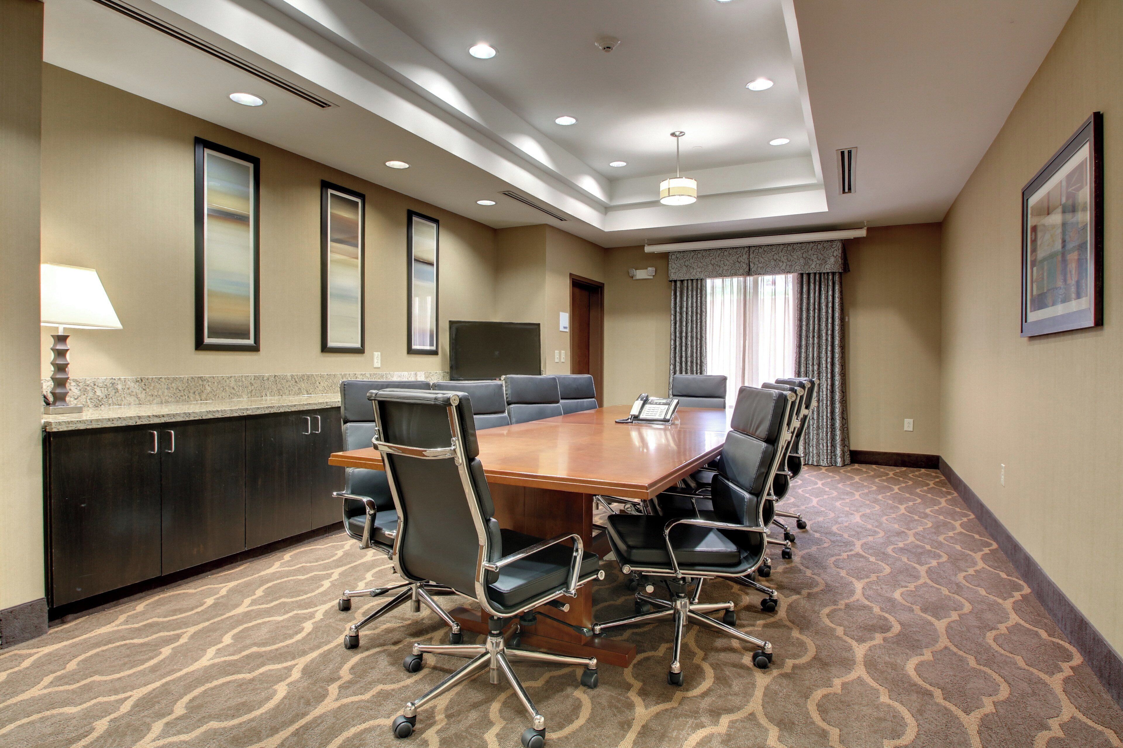 A conference room with a large table, chairs, a lamp, and framed pictures on the wall.