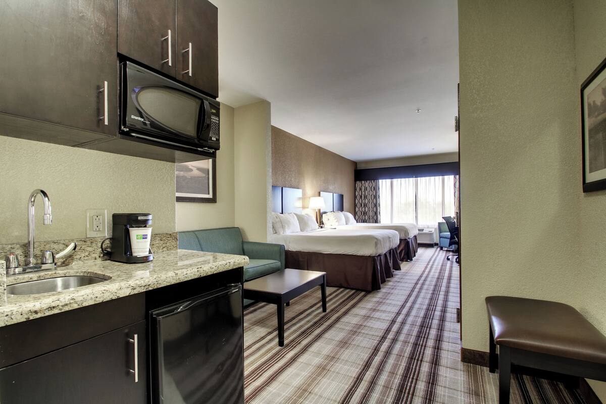A hotel room with a kitchenette, a bed, a sofa, a desk, and a bathroom.