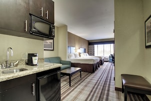 A hotel room with a kitchenette, a bed, a sofa, a desk, and a bathroom.