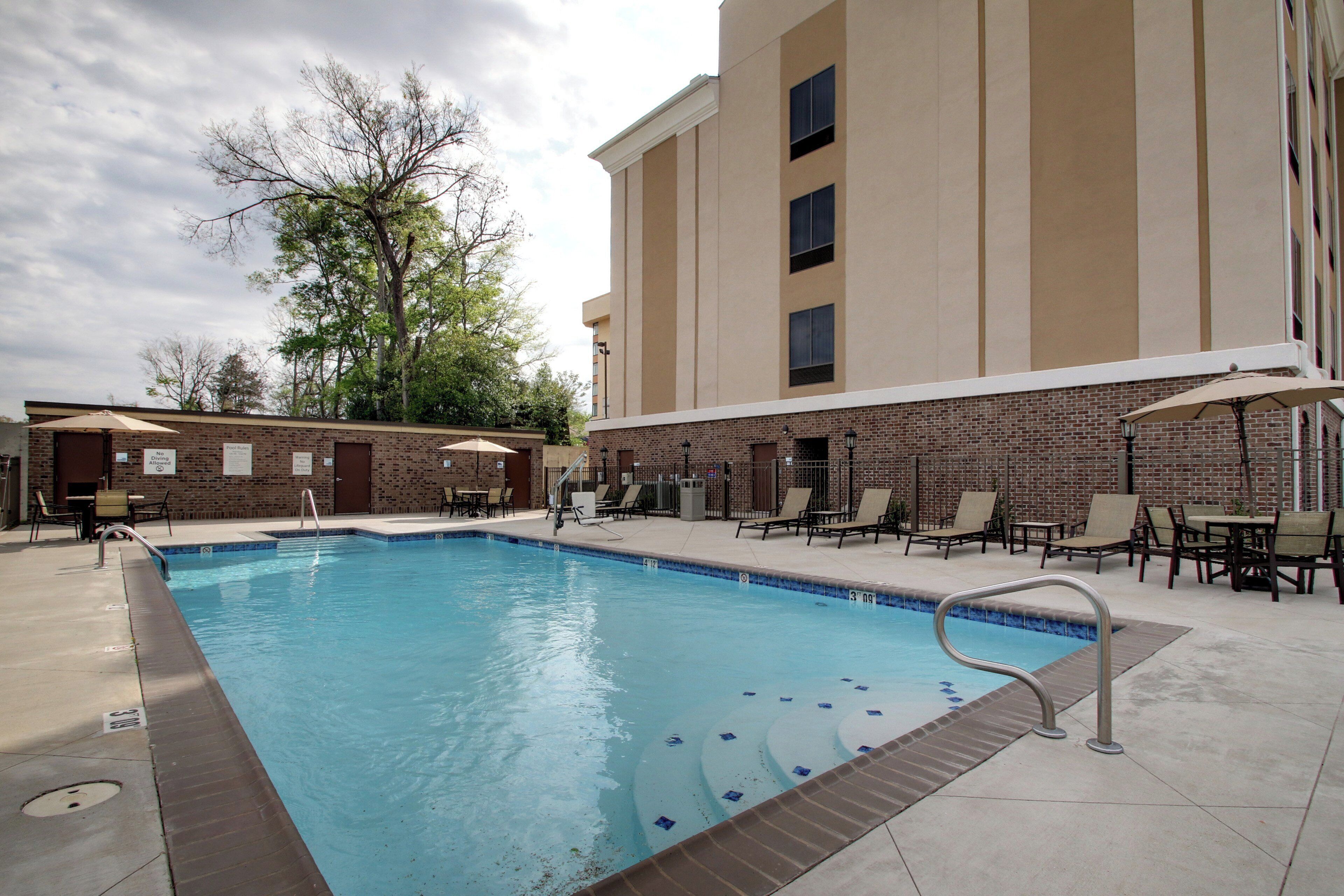 A swimming pool with lounge chairs and umbrellas, surrounded by a brick building with multiple windows.