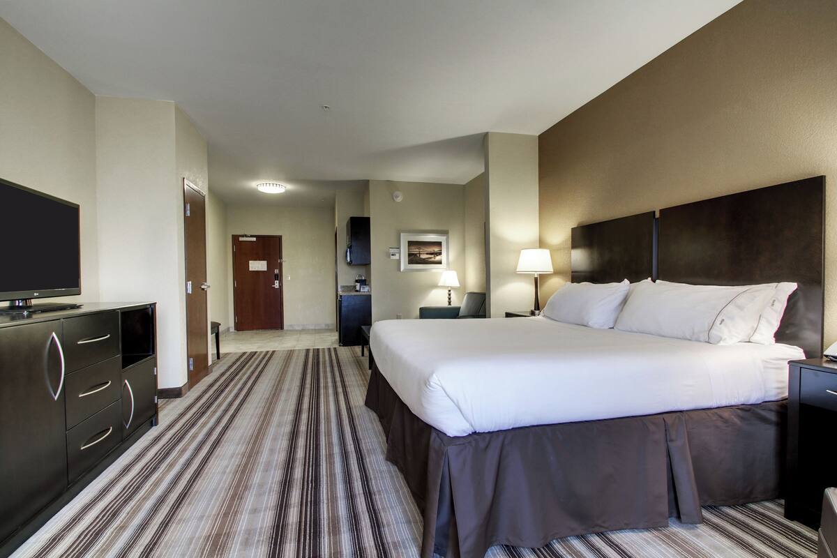 A hotel room with a large bed, a flat-screen TV, a desk with a lamp, and a carpeted floor.