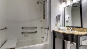 A modern bathroom with a bathtub, a vanity with a mirror, and a hairdryer mounted on the wall. - Holiday Inn Express Hotel & Suites Natchez South by IHG (Natchez)