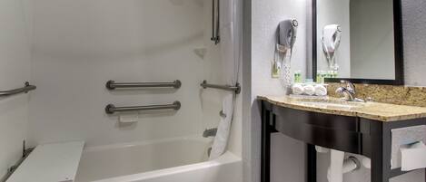 A modern bathroom with a bathtub, a vanity with a mirror, and a hairdryer mounted on the wall.