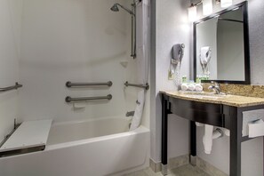 A modern bathroom with a bathtub, a vanity with a mirror, and a hairdryer mounted on the wall. - Holiday Inn Express Hotel & Suites Natchez South by IHG (Natchez)