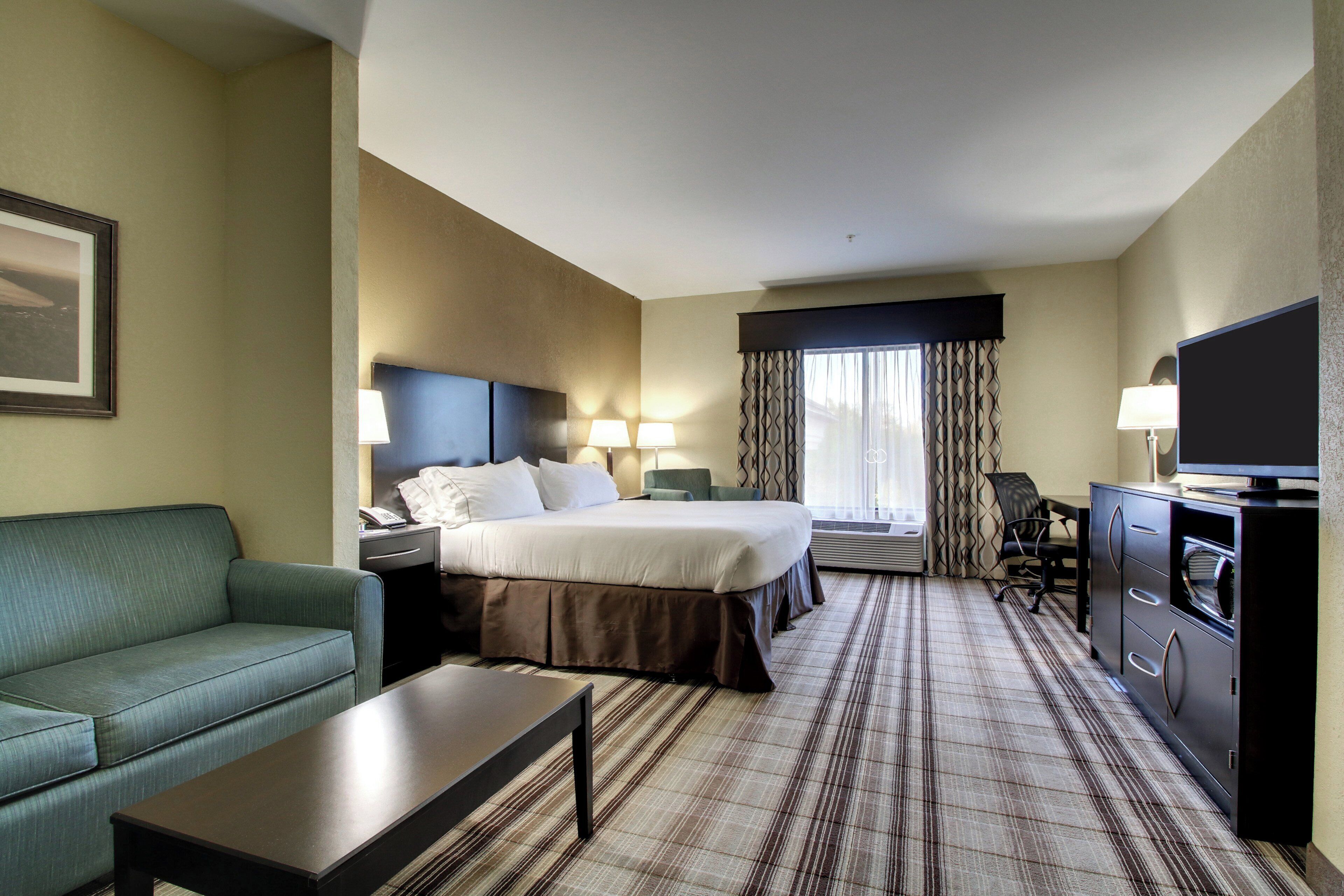 A hotel room with a bed, a sofa, a desk, a television, and a window with curtains.