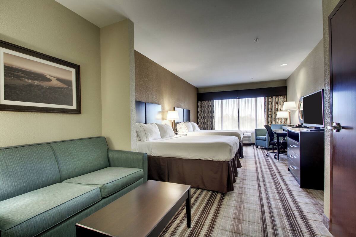 A hotel room with a green sofa, two beds, a desk, a TV, and a framed picture on the wall.