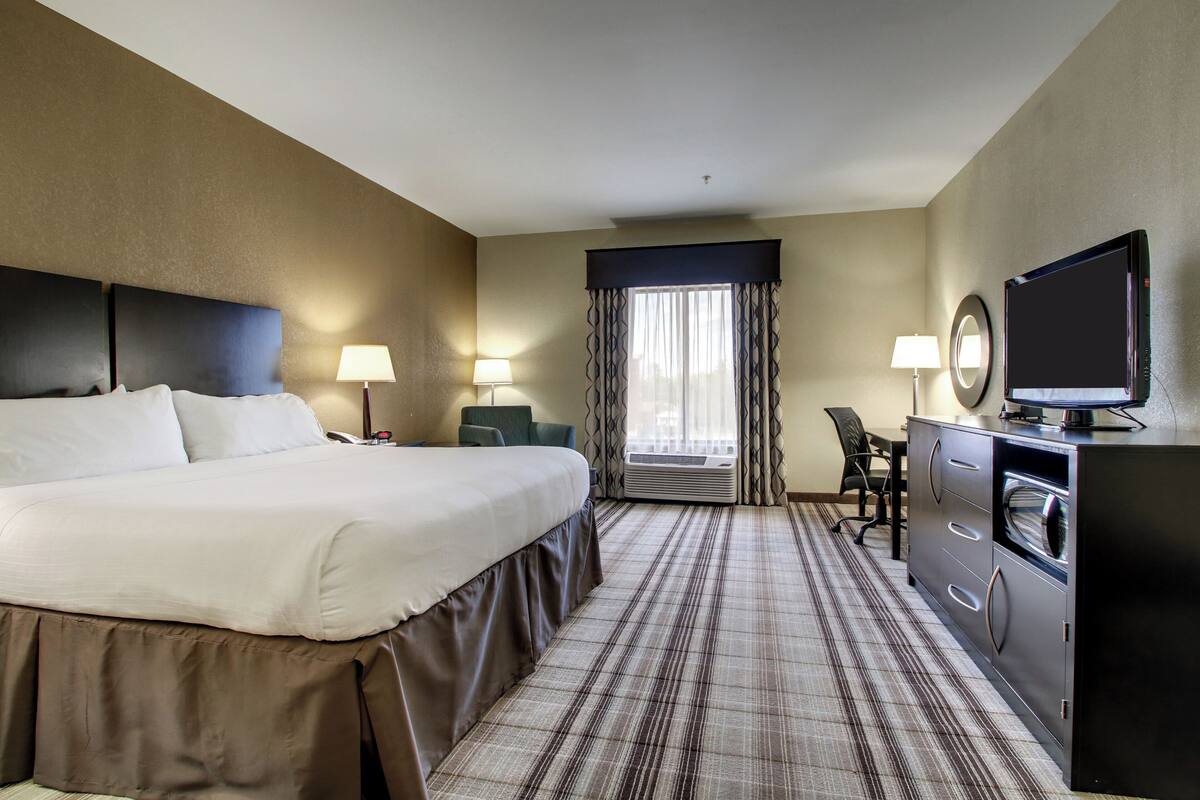 A hotel room with a large bed, a desk with a chair, a television, and a dresser.