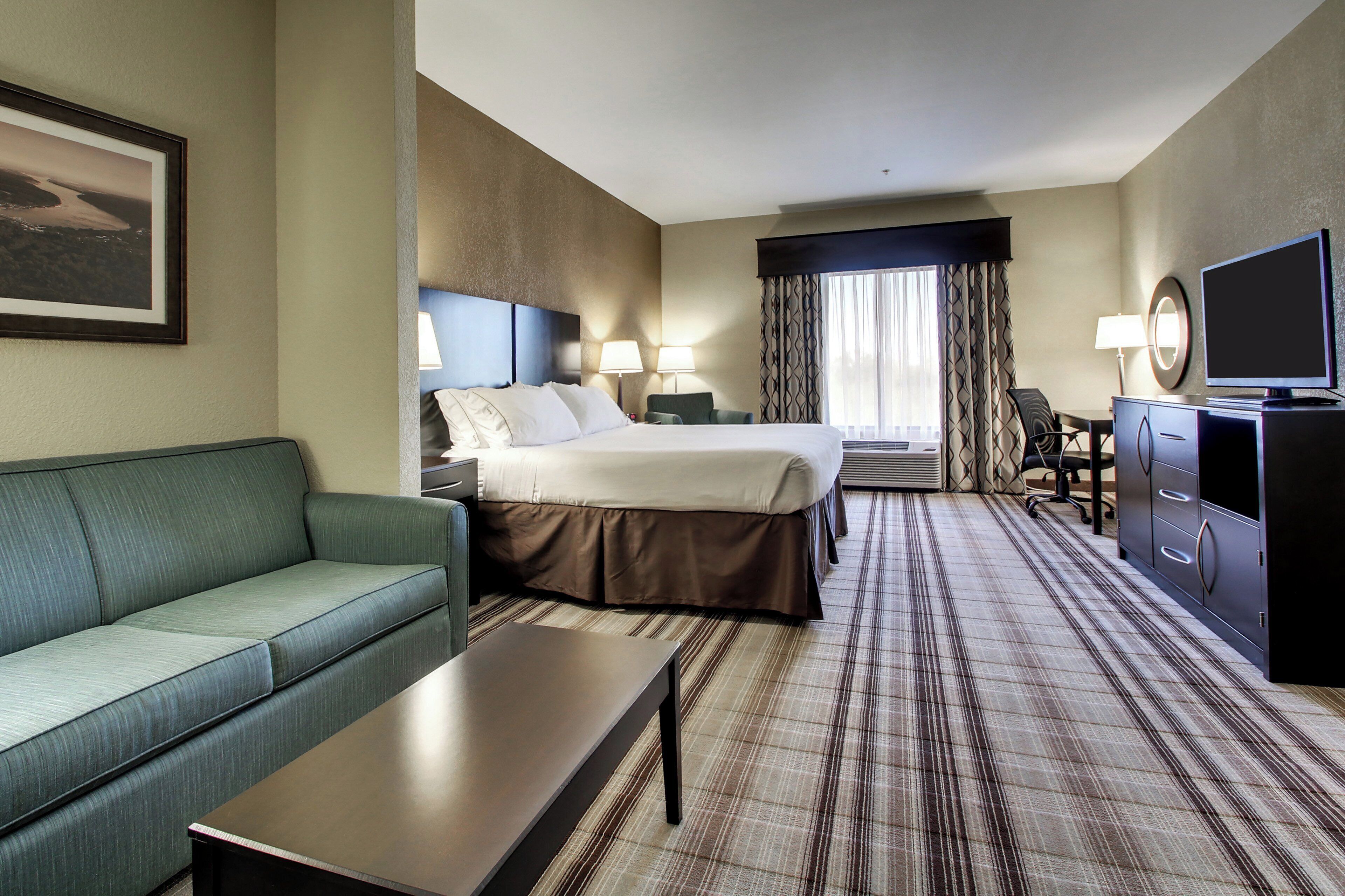 A hotel room with a bed, a sofa, a desk, a TV, and a window with curtains.