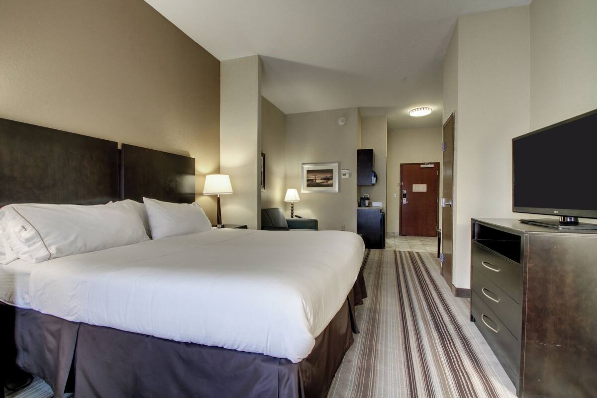 A hotel room with a large bed, bedside tables, a TV, a desk, and a lamp.