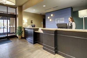 A hotel reception desk with a receptionist, a plant, and a sign for Holiday Inn Express. - Holiday Inn Express Hotel & Suites Natchez South by IHG (Natchez)