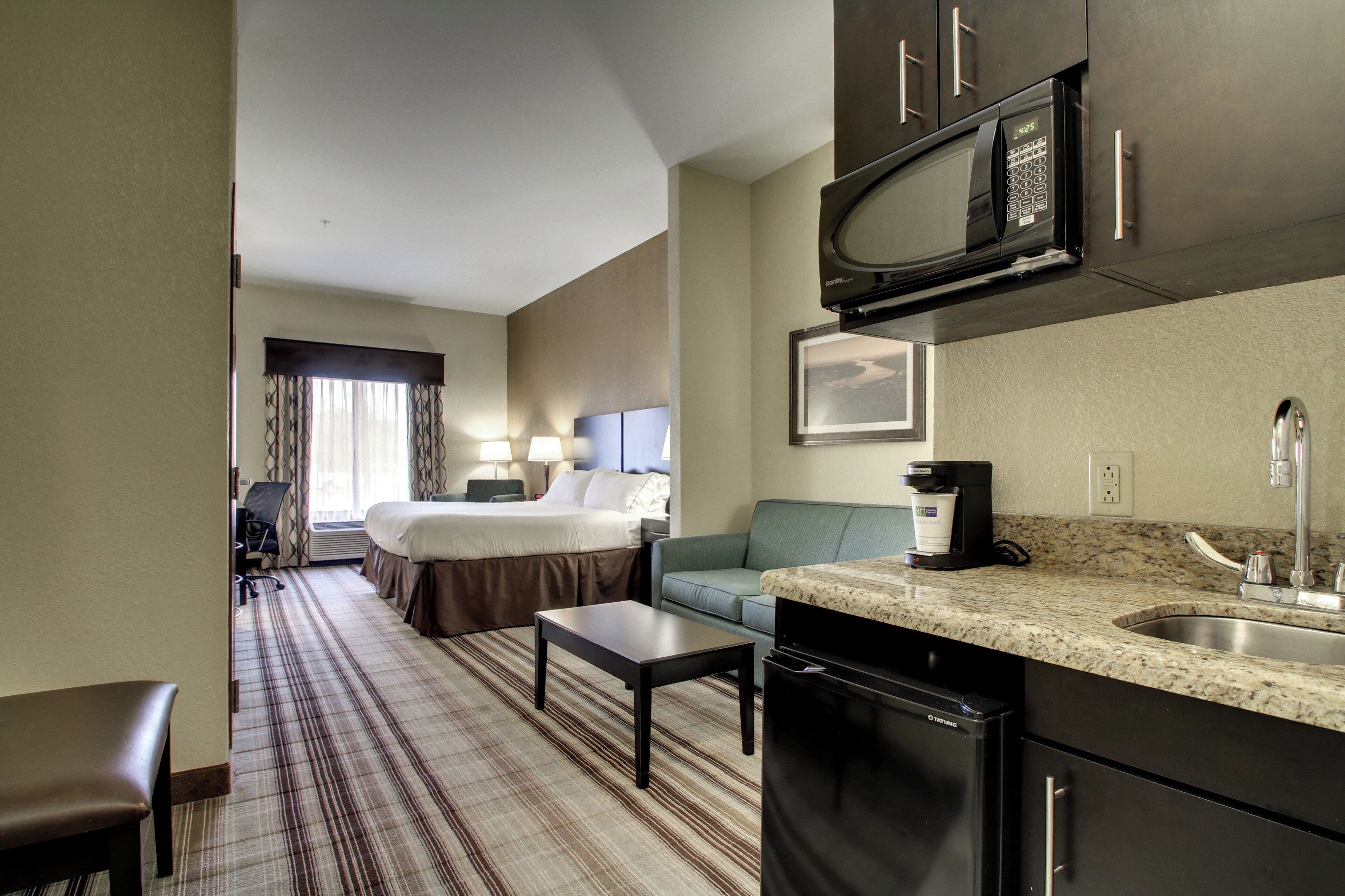 A hotel room with a bed, a sofa, a coffee maker, a microwave, and a sink.