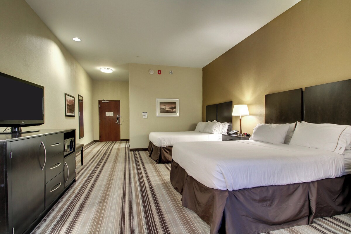 A hotel room with two beds, a TV, a desk, and a lamp.