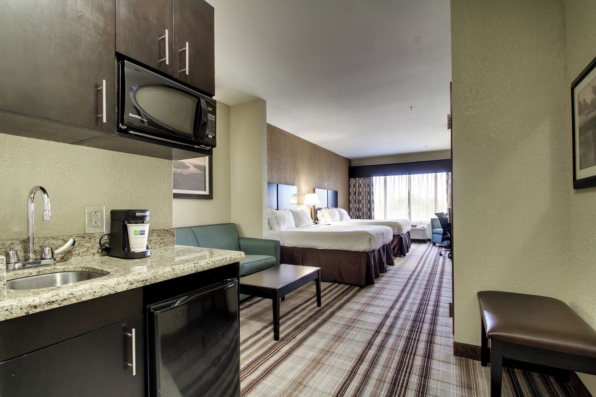 A hotel room with a kitchenette, a bed, a seating area, and a view of the hallway.
