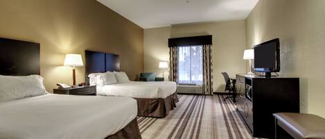 A hotel room with two beds, a desk with a television, a chair, and a window with curtains.