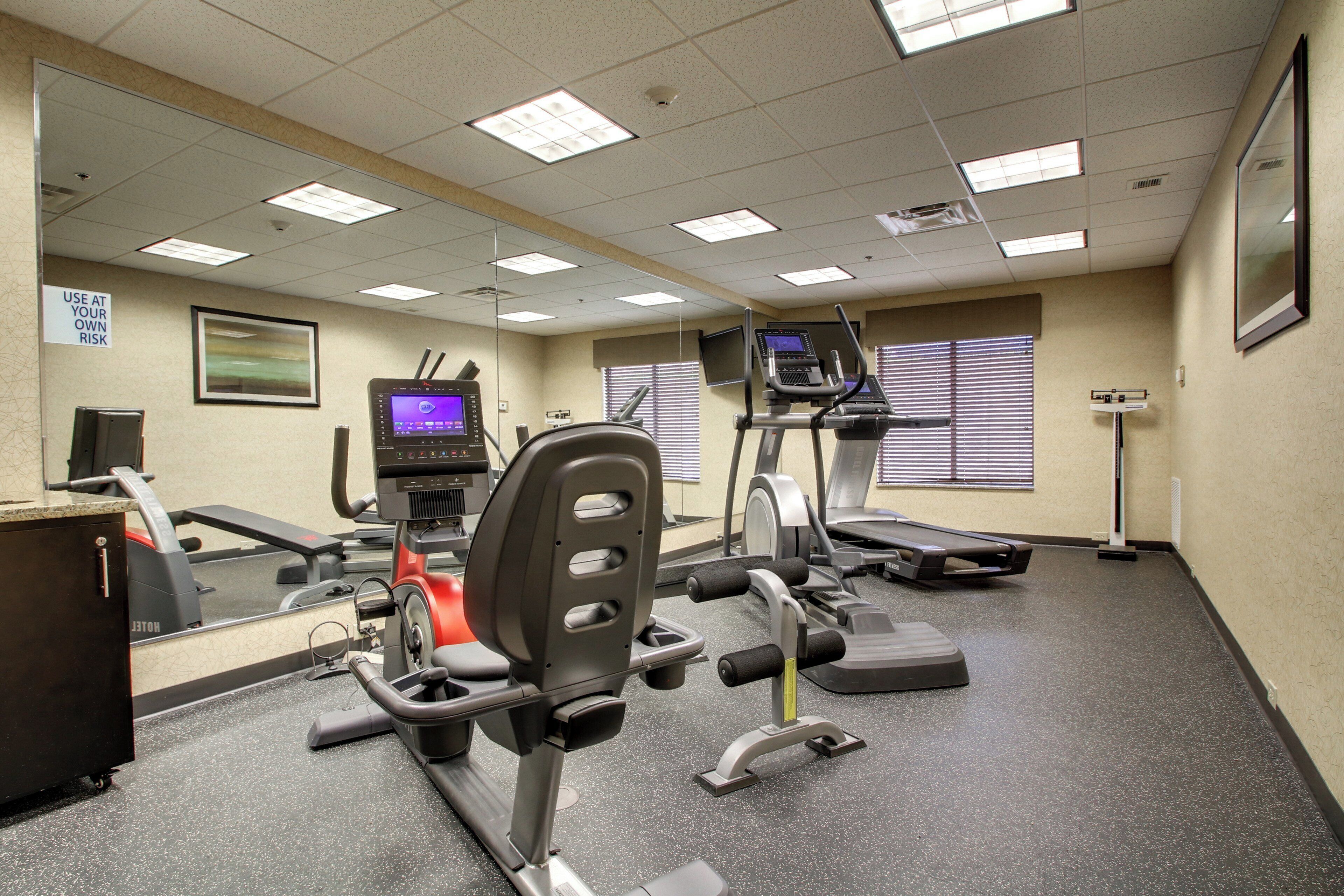 A gym with exercise equipment, a television, and a sign warning to use equipment at your own risk.