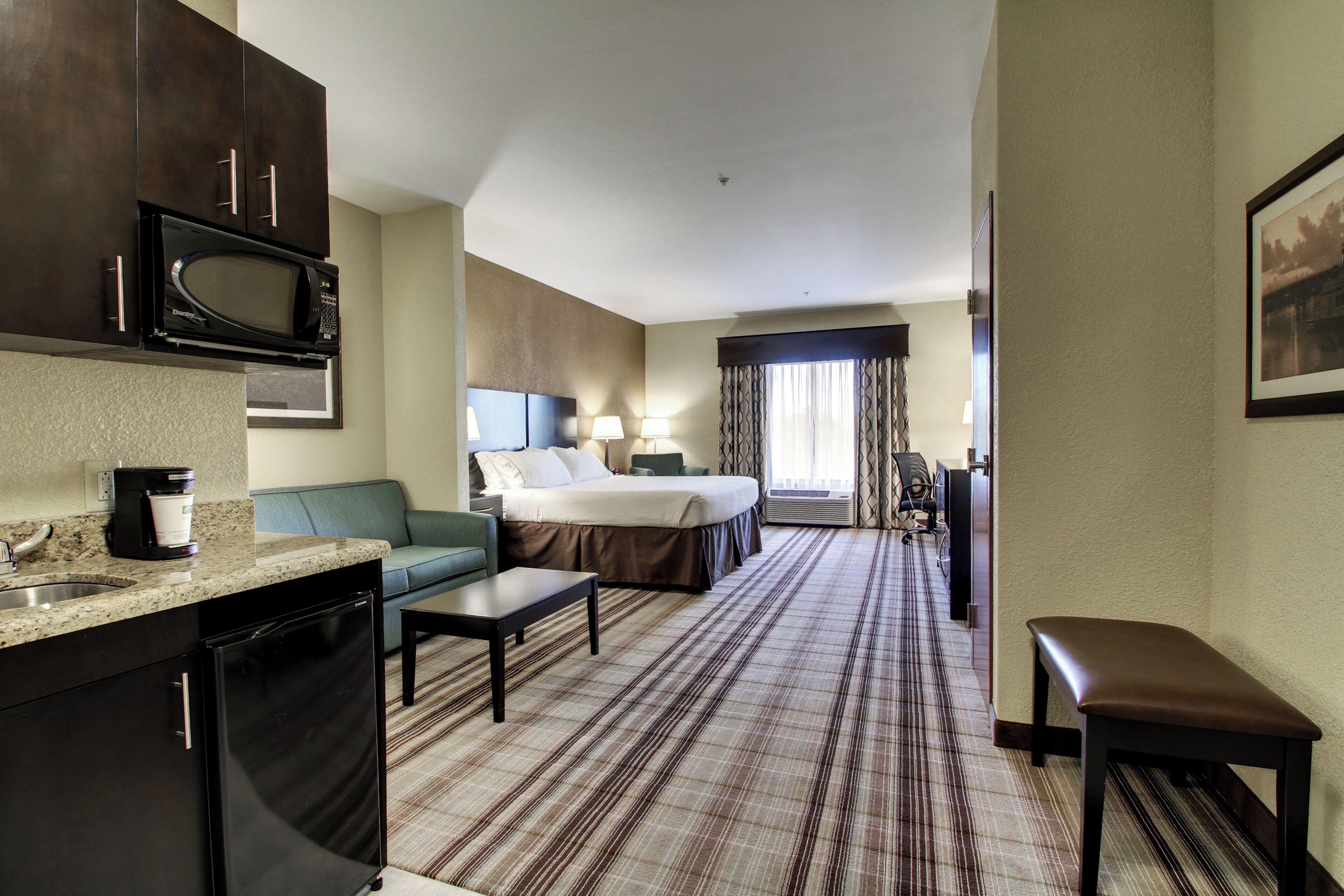 A hotel room with a kitchenette, a bed, a sofa, a desk, and a bathroom.