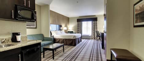 A hotel room with a kitchenette, a bed, a sofa, a desk, and a bathroom.