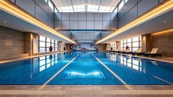 Uma grande piscina interior com chão em mosaico, teto iluminado pelo sol e um mural de golfinhos na parede.