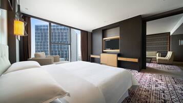 Quarto de hotel moderno com uma cama grande, TV, escrivaninha e vista para a cidade.