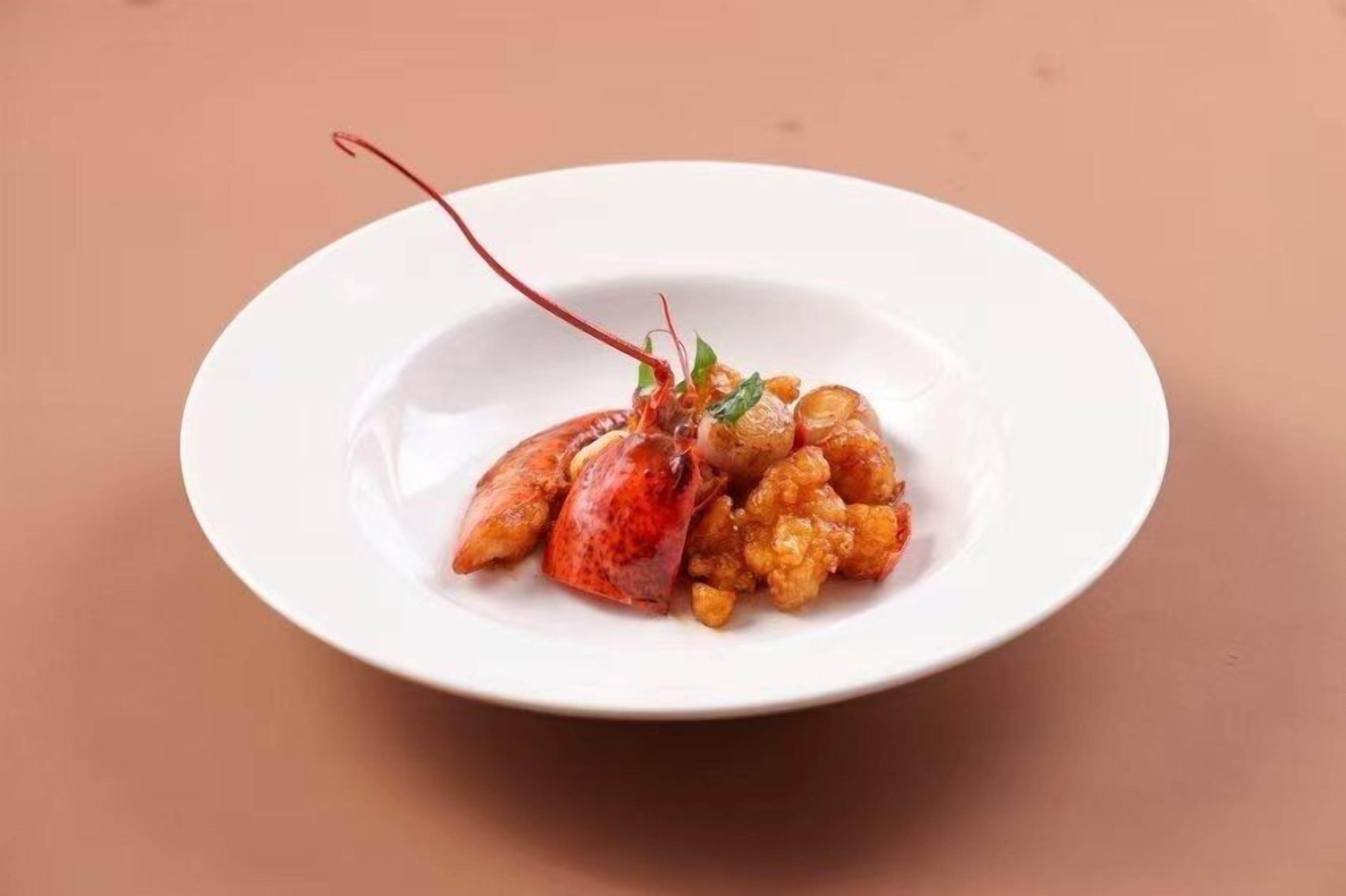 Un plato blanco con una cola de langosta y comida sobre una mesa.