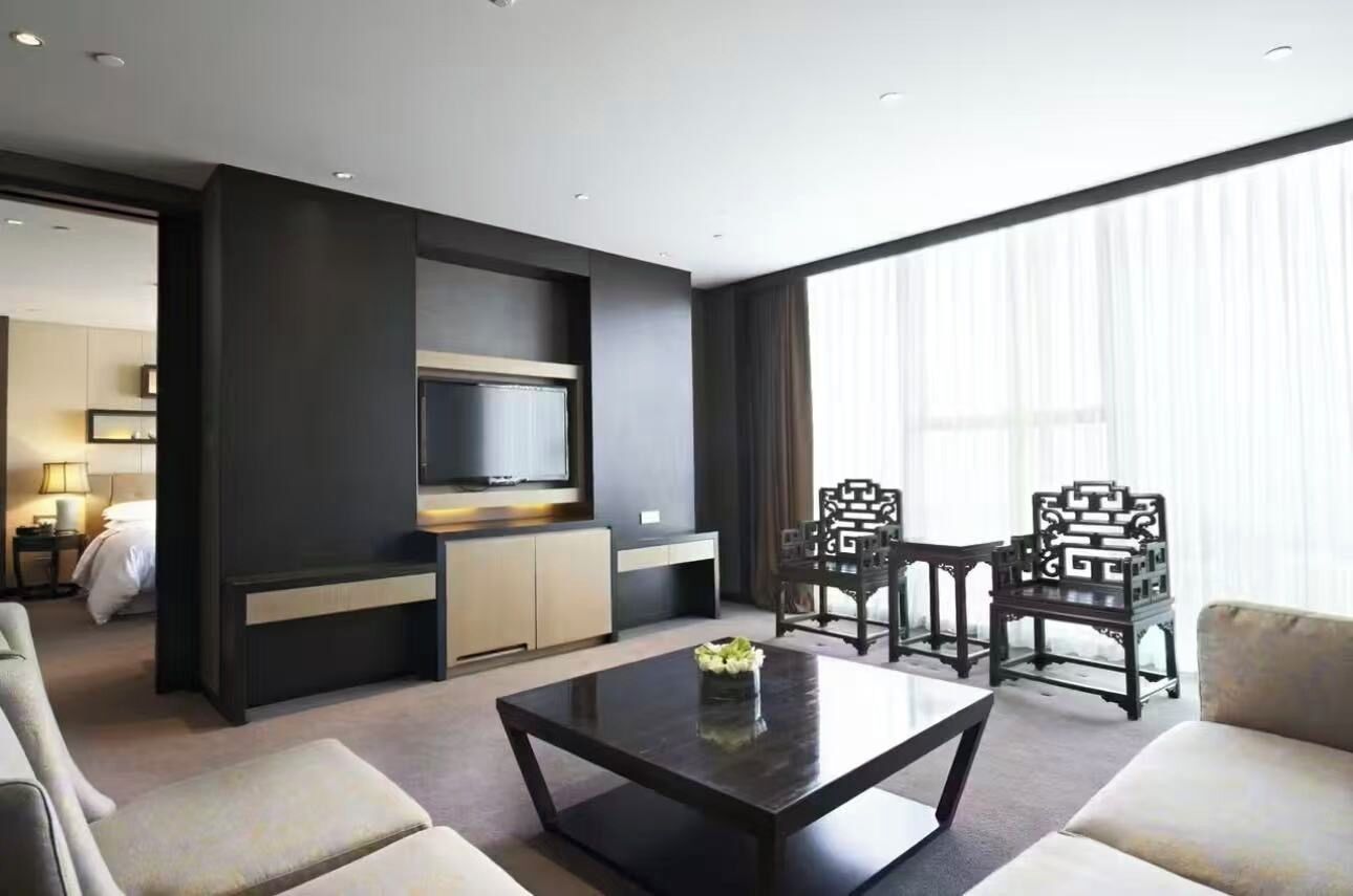 Ein modernes Hotelzimmer mit Flachbildfernseher, einer Couch, einem Couchtisch und traditionellen Sesseln.