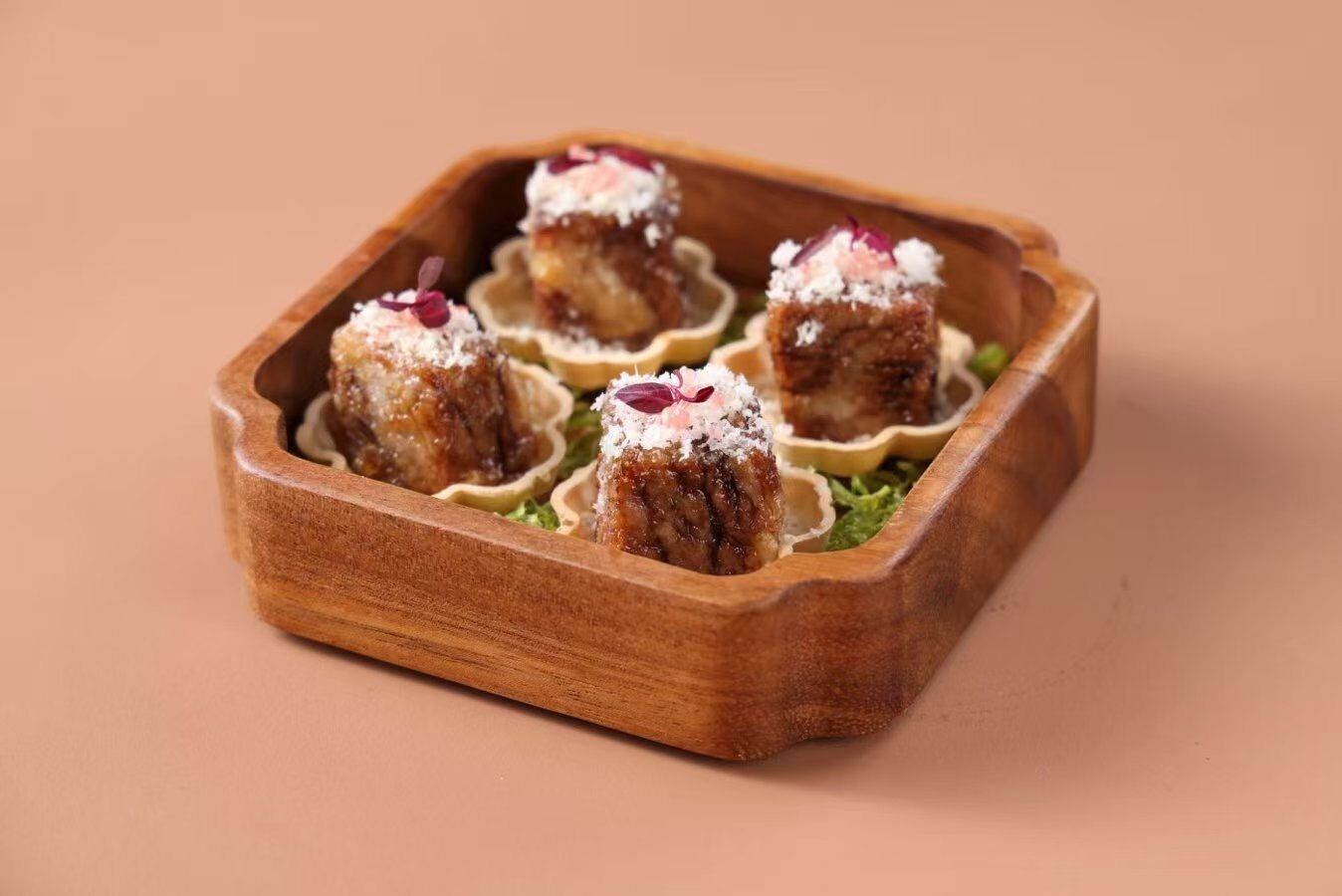 A wooden tray with four food items, each in a shell-like container, on a plain background.