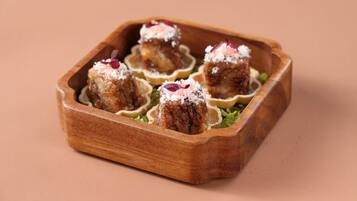 A wooden tray with four food items, each in a shell-like container, on a plain background.