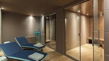 A modern spa area with two reclining chairs, a glass-enclosed shower, and a wooden floor.