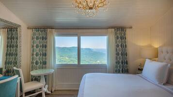 A hotel room with a large bed, a chandelier, a small table, and curtains.