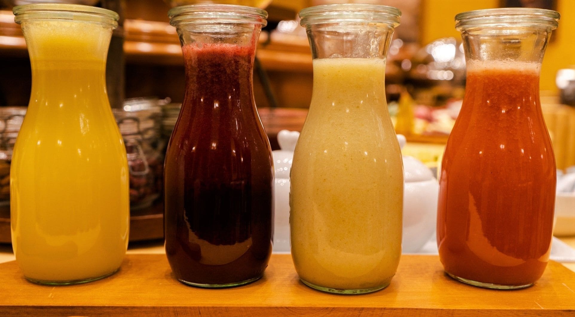Four glass bottles with different colored beverages on a wooden surface.