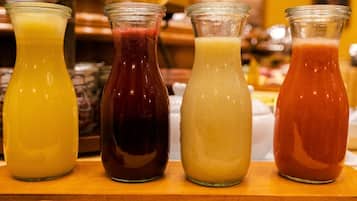Fyra glasflaskor med drycker i olika färger, placerade på en träyta.