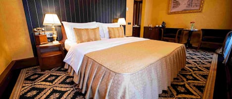 A hotel room with a large bed, two bedside tables with lamps, a small table with a vase, and a patterned carpet.