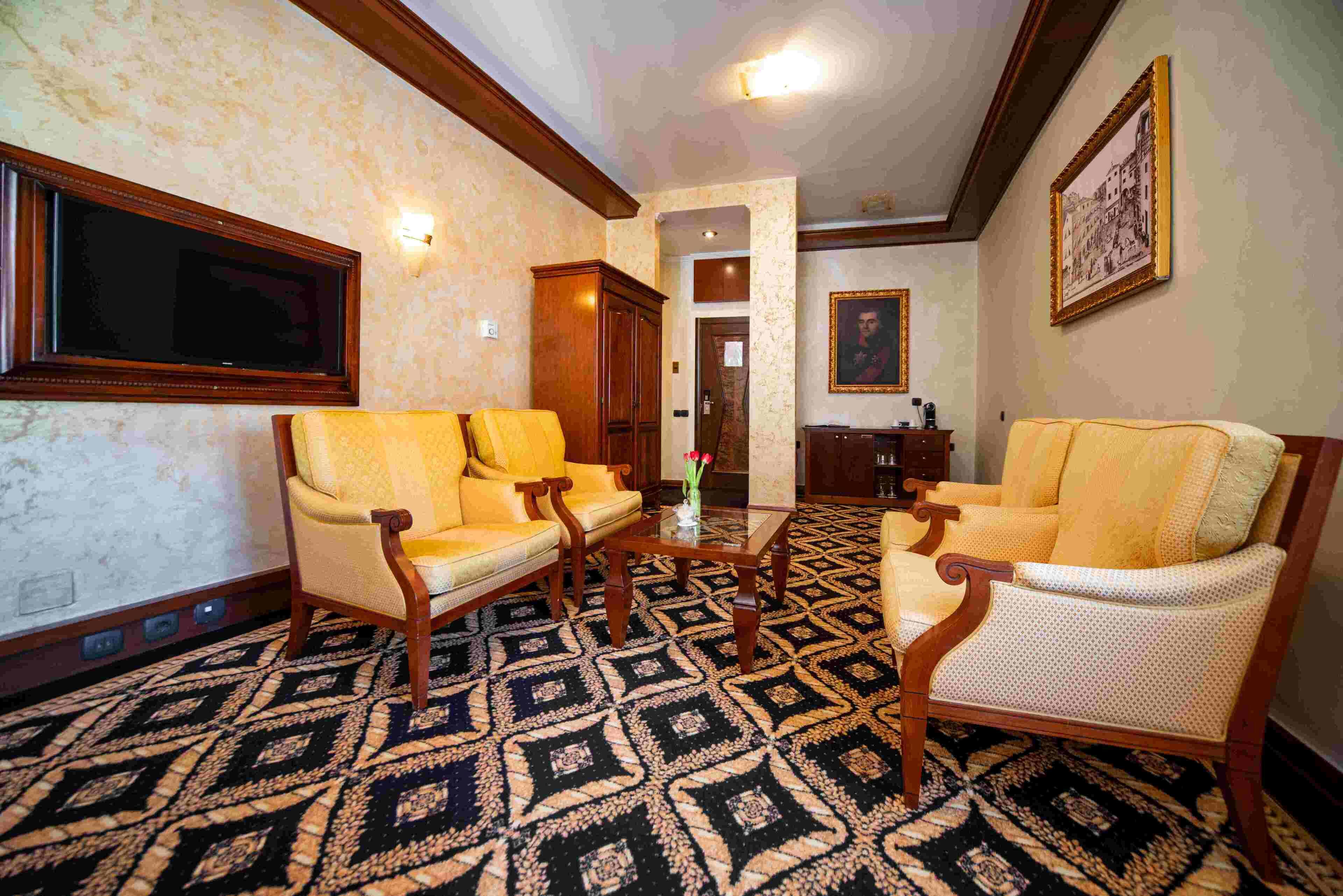 Una habitación con dos sillones amarillos, una mesa de centro de madera, alfombra estampada y un cuadro en la pared.