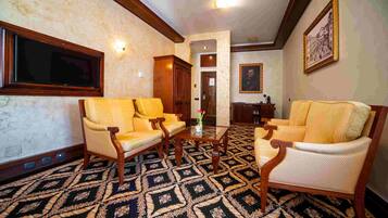 Una habitación con dos sillones amarillos, una mesa de centro de madera, alfombra estampada y un cuadro en la pared.