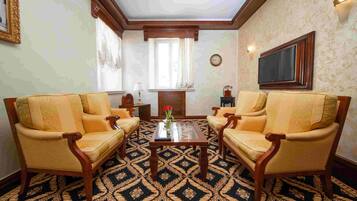 A room with two armchairs, a small table, a clock, and a television on the wall.