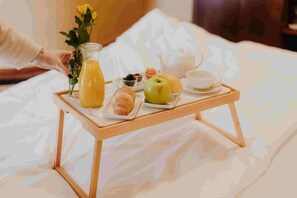A breakfast tray with a bottle of orange juice, a green apple, croissants, and pastries on a bed.