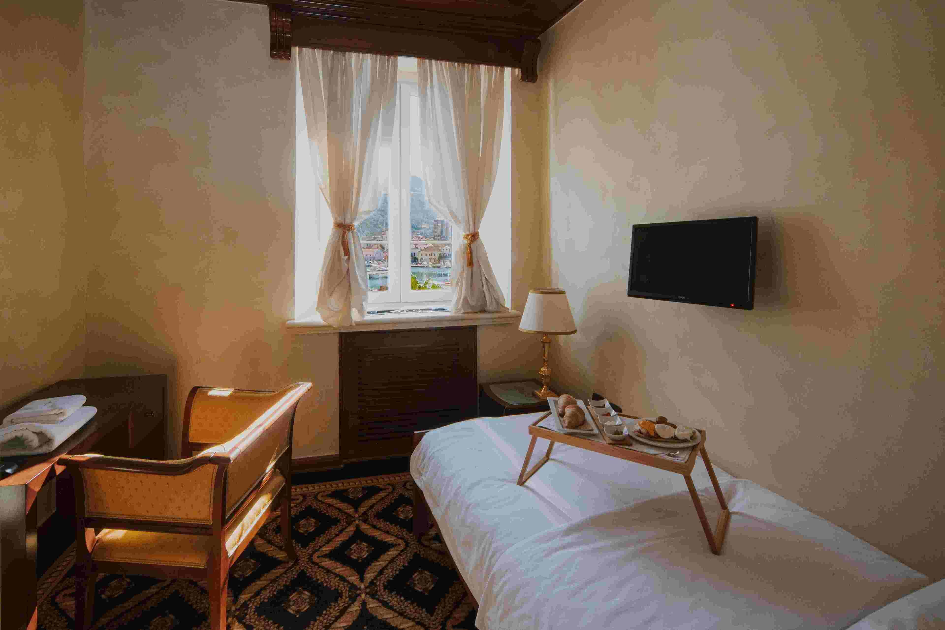 A hotel room with a bed, a desk, a chair, a lamp, and a TV.
