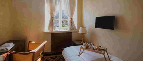 A hotel room with a bed, a desk, a chair, a lamp, and a TV.