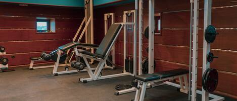 A gym with weightlifting equipment, benches, and a mirror.