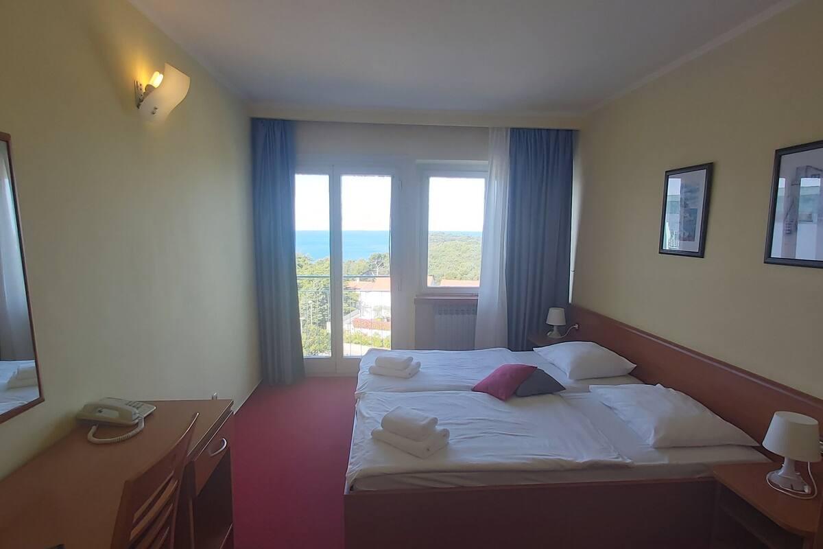 Habitación de hotel con cama, escritorio, teléfono y vistas al mar.
