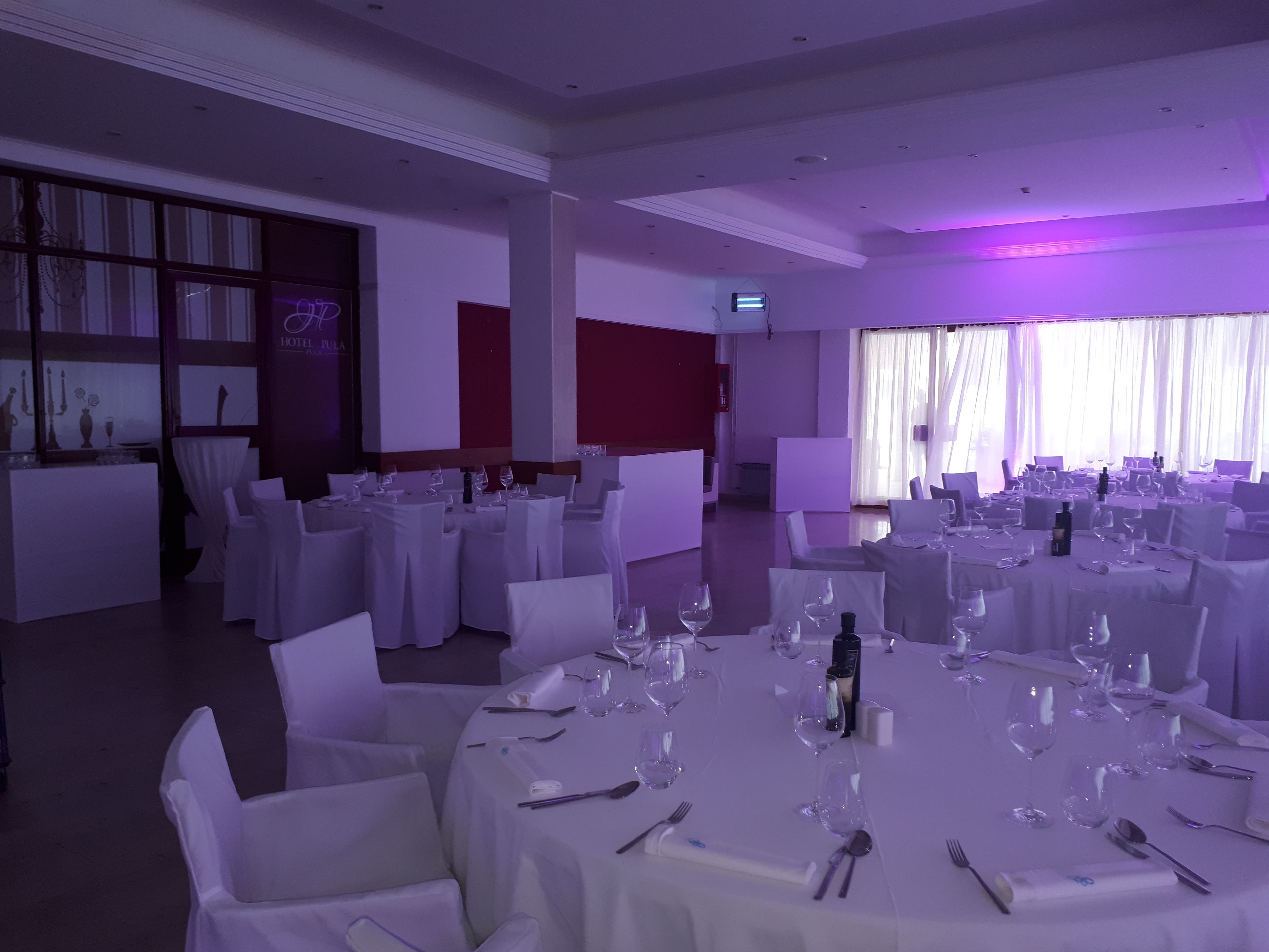 A banquet hall with round tables set for dining, white chairs, and a modern interior design.