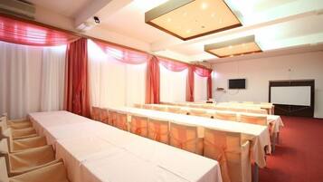 Un salón de conferencias con una larga mesa, sillas, una pantalla de proyector y una pizarra.
